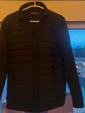 Svart cardigan från Dressman - Svart cardigan från Dressman med quiltad framsida och slät rygg. Jackan har dragkedja framtill, hög krage och långa ärmar. Perfekt för kalla dagar när du vill hålla värmen och ändå se stilren ut. Hör av dig om du är intresserad av något! 🙂