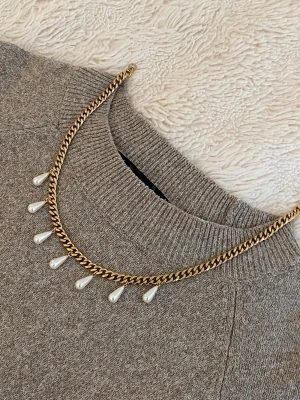 Guldfärgat halsband med pärldroppar - Stilrent halsband i guldfärgad rostfritt med kedja och sju droppformade pärlor som hänger längs framsidan. Perfekt accessoar för att lyfta din outfit med en elegant touch.