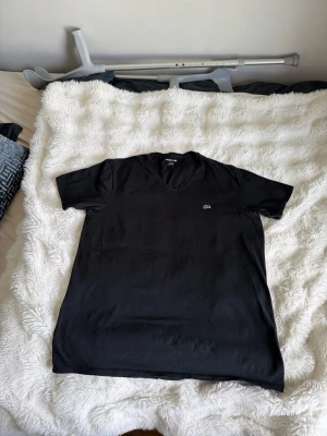 Svart v-ringad t-shirt från Lacoste - Svart t-shirt från Lacoste med v-ringning och klassisk krokodillogga på bröstet. T-shirten är kortärmad och har en clean, stilren look som passar till det mesta. Tillverkad i mjuk bomull för skön känsla hela dagen.