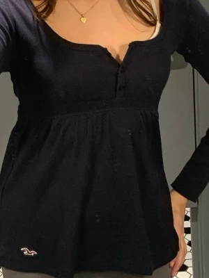 Mörkblå långärmad blus Hollister - Supersöt mörkblå blus från Hollister med lång ärm, knappar framtill och markerad midja med knytband. Tillverkad i mjuk bomull och har en liten logga broderad nertill. Perfekt för dig som gillar en enkel men ändå feminin stil. Storlek M men passar S💗