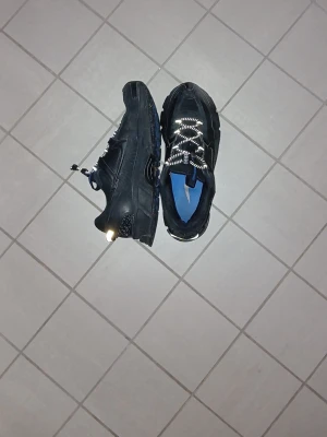 Svarta Nike sneakers med blå sula - Nike Zoom Vomero Roam – Svarta – Mycket fint skick  Säljer ett par Nike Zoom Vomero Roam i svart. Endast sparsamt använda och i mycket fint skick. Skorna kombinerar komforten från Nike Zoom Vomero-serien med en mer robust design som passar både streetwear och utomhusbruk. De är byggda för kallare väder och fungerar utmärkt för promenader, vardagsbruk och lättare vandring. Modellen är framtagen för att klara vinterförhållanden och temperaturer ner mot cirka -20°C.  • Nike Zoom Vomero Roam • Färg