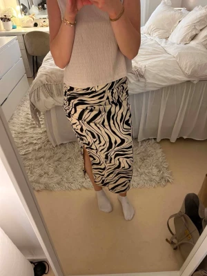 Zebramönstrad långkjol med slits - Säljer en snygg långkjol med zebramönster i svart och vitt. Kjolen har en slits på sidan som ger en trendig touch och är perfekt för dig som gillar att sticka ut. Materialet känns mjukt och följsamt mot kroppen.
