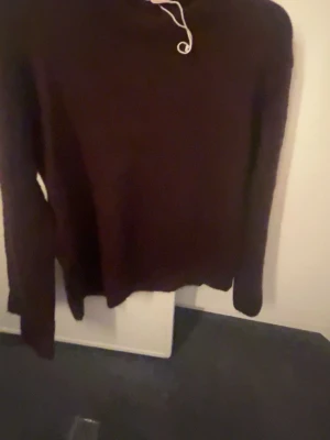 Vinröd stickad tröja - Mysig mörkbrun stickad tröja med rund hals och långa ärmar. Tröjan har en enkel och stilren design med ribbade muddar vid ärmslut och nederkant. Perfekt för kalla dagar och lätt att matcha med olika outfits.