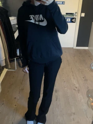 Svart Nike hoodie - Svart hoodie från Nike med stor vit logga framtill. Klassisk modell med huva och känguruficka. Mjuk och skön, passar till det allt!
