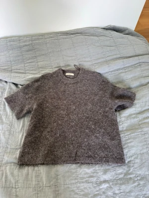 Brun fluffig stickad tröja kort ärm - Mysig brun stickad tröja med korta ärmar och rund hals. Tröjan har en fluffig, mjuk yta och rak passform. Perfekt för lager på lager och enkel att styla till olika outfits.