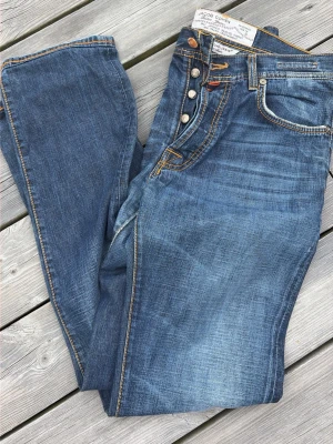 Blå jeans från Jacob Cohen - Snygga blå jeans från Jacob Cohen med gul kontrastsöm och broderad J på myntfickan. Klassisk femficksmodell med knappgylf och slitna detaljer för en avslappnad look. Tillverkade i mjukt denimtyg som sitter skönt hela dagen.
