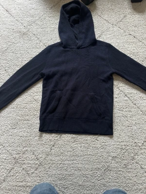 Svart/mörkblå cashmir hoodie Ralph lauren  - En stilren svart/mörklblå cashmir hoodie från polo Ralph lauren med klassisk huva och stor magficka framtill. Hoodien har långa ärmar och ribbade muddar vid ärmslut och nederkant. Perfekt för en avslappnad och enkel look. Materialet känns mjukt och bekvämt mot huden. Storlek 14-16 år 