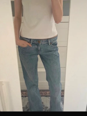 Blå raka jeans med låg midja - Säljer ett par klassiska blå jeans med rak passform och låg  midja. Jeansen har fem fickor, bälteshällor och stängs med knapp och dragkedja. Tillverkade i denim. 