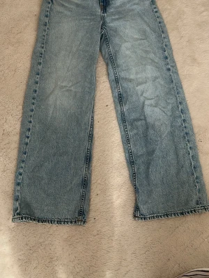 Blå raka jeans från Kappahl - Ett par ljusblå raka jeans från Kappahl son är vida och klassisk femficksmodell. Jeansen har en avslappnad passform och är tillverkade i denim med tydliga sömmar. 