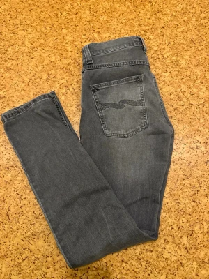 Nudie Jeans Lean Dean - Säljer ett par gråa slim fit jeans från Nudie Jeans med klassisk femficksmodell och snygga slitningar. Jeansen har en diskret logga på bakfickan och är tillverkade i mjuk bomullsdenim. Perfekta för en avslappnad och trendig look.