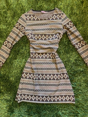 Mönstrad långärmad midi cocktail dress - Snygg och festlig mönstrad långärmad cocktail midi-klänning med geometriskt mönster i beige, svart och guld. Klänningen har rund halsringning och figurnära passform. Perfekt för dig som gillar unika prints och vill sticka ut lite extra.