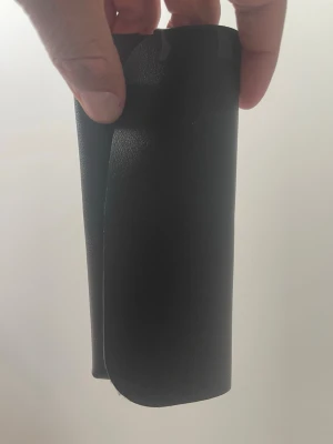 Svart minimalistisk plånbok i skinn - En stilren svart plånbok i minimalistisk design, tillverkad i slätt skinnliknande material. Plånboken har rundade hörn och ett praktiskt band som håller den stängd. Perfekt för dig som gillar enkel och modern stil.