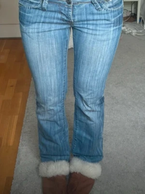 Ljusblå bootcut jeans - Säljer ett par ljusblå bootcut jeans med snygga slitningar och klassiska fickor bak. Jeansen har låg midja och är i mjukt denimtyg. Perfekta för dig som gillar en avslappnad och trendig look. Lånade bilder🩷