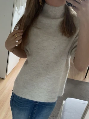 Beige stickad tröja från Gina Tricot  - Beige stickad tröja med halvpolokrage och korta ärmar. Tröjan har en rak passform och ribbade avslut vid ärmar och nederkant. Tröjan är från Gina Tricot i storlek xs.