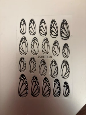 Nail art sticker - Nagelstickers med svart fjärilsvinge-design i olika storlekar. Perfekt för att skapa unika och kreativa nagellooks. Klistermärkena är genomskinliga med svarta detaljer och passar både långa och korta naglar.