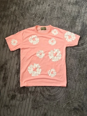 Rosa t-shirt med vita blommor - Säljer en rosa t-shirt med vita blommönster på både fram- och baksidan. T-shirten har korta ärmar och en avslappnad passform. Perfekt för dig som vill sticka ut med en färgglad och unik stil. Står att den passar s men det passar n och nästan L
