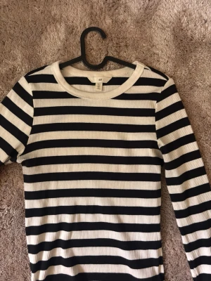 Randig ribbad topp från H&M - Säljer en svartvit ribbad topp från H&M med klassiskt randigt mönster och rund halsringning. Toppen har långärmad passform och är tillverkad i mjukt material som sitter bekvämt. Perfekt för dig som gillar stilrena och enkla plagg.