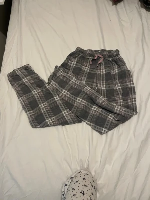 Rutiga pyjamasbyxor med dragsko - Mysiga pyjamasbyxor i grått och vitt rutigt mönster med rosa dragsko i midjan. Byxorna har resår i midjan och är tillverkade i mjukt, flanell-liknande material. Perfekta för chillkvällar hemma💕.