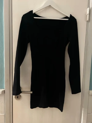 Svart långärmad kortklänning - En enkel och stilren svart kortklänning med lång ärm och figurnära passform. Klänningen har en rak, något tight siluett och är tillverkad i ett stretchigt material som formar sig efter kroppen. Perfekt för dig som gillar minimalistisk och klassisk stil. Tyget är ribbat och har ”tummy control”