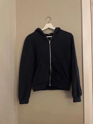 Mörkblå zip hoodie med huva - En enkel mörkblå hoodie med dragkedja framtill och två fickor. Klassisk modell med huva och ribbade muddar vid ärmar och nederkant. 