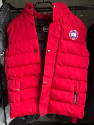 Röd dunväst från Canada Goose - Snygg röd dunväst från Canada Goose ej äkta! Det står S men passar perfect for dig som bär STORLEK M