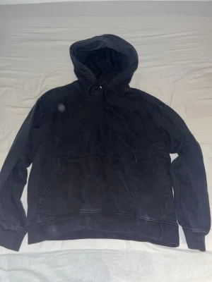 Svart hoodie VAILENT - En klassisk svart hoodie från vailent med huva och dragsko samt en stor magficka framtill. Hoodien har ribbade muddar vid ärmslut och nederkant. Perfekt för en avslappnad och stilren look. Haft den ett tag så svarta färgen har blivit liksom lite nedsliten och särför fått en nästan vintage look. Tröjan är baggy fit.