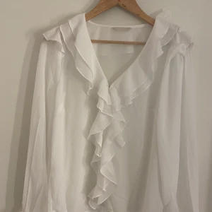 Vit blus med volanger  - En så fin blus från Ellos! Helt ny. Tyvärr saknas lapp. Kan upplevas lite stor och är ganska genomskinlig
