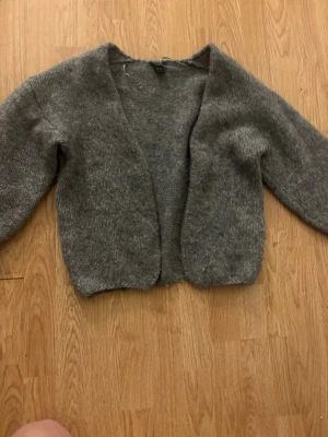 Grå stickad kofta i mjukt material - Mysig grå stickad kofta med öppen front. Koftan har en avslappnad passform och är tillverkad i ett mjukt, fluffigt material som känns skönt mot huden. Perfekt att slänga på sig över en t-shirt eller topp.