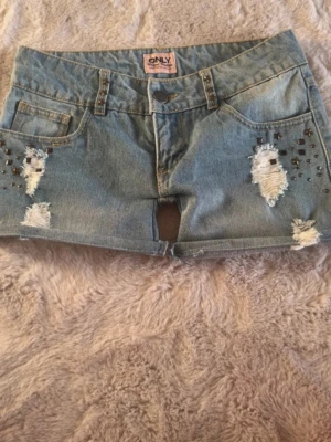 Blå jeansshorts med nitar från ONLY - Snygga blå jeansshorts från ONLY med slitna detaljer och snygga metall detaljer på bakfickor och där fram. Klassisk shortsmodell med låg midja de är insydda vid låren. Perfekta för sommaren och är super snygga! 42 cm runt låren i omkets, från höft till lår 27cm, 78 cm i midjan i omkets. Fråga om ni undrar något!!💕