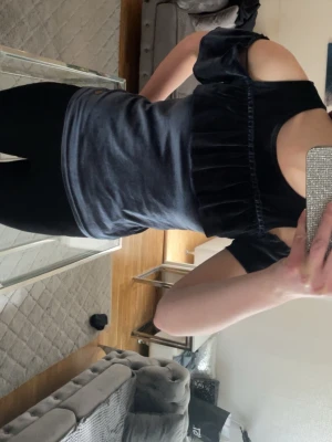 Mörkblå sammets topp med volang - Snygg mörkblå sammets topp med volangdetalj över bröstet och trendiga offshoulder-ärmar. Perfekt för dig som vill sticka ut med en cool och mjuk look. Toppen har en figurnära passform och känns lyxig tack vare det glansiga materialet.