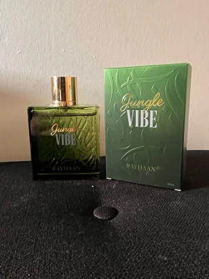 Jungle Vibe parfym från Rayhaan - Jungle Vibe är en parfym från Rayhaan med en grön, fyrkantig glasflaska och guldfärgad kork. Förpackningen har ett djungelinspirerat mönster och text i vitt och guld. Perfekt för dig som vill ha en unik och fräsch doft.