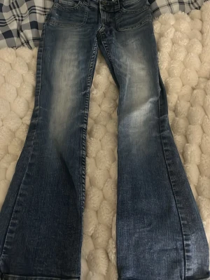 Blå bootcut jeans med slitningar från HM - Säljer ett par blå bootcut jeans med snygga slitningar och tvättade detaljer. Jeansen har klassiska fem fickor och knappar bak på fickorna. Perfekta för dig som gillar retrostil och vill ha ett par jeans med lite vidare ben. Har en liten skrapa som man kan se på bild tre med den är pytte liten och är inte hela vägen igenom, själv tycker jag att det ser ut som att det ska vara så.😋😋
