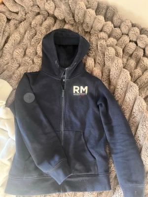 Race marine hoodie - Snygg marinblå hoodie från race marine med dragkedja, huva och RM-tryck på bröstet. Hoodien har en patch på ärmen och praktiska fickor framtill. Nästan helt oanvänd vet inte om de är tjej eller kill modell men är snygg på båda ja och min bror har delat, storlek 146,152!
