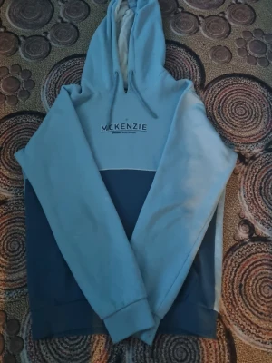 Blå hoodie från McKenzie - Snygg hoodie från McKenzie i två nyanser av blått med vit insida på huvan. Hoodien har dragsko i huvan och tryckt logga på bröstet. Perfekt för dig som gillar en avslappnad och sportig stil.