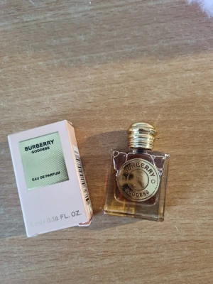 Burberry Goddess Eau de Parfum - Burberry Goddess Eau de Parfum i en liten, lyxig glasflaska med guldfärgad metallkork och detaljer. Flaskan är transparent med en elegant rund etikett framtill. Medföljer originalkartong i ljusrosa nyans.
