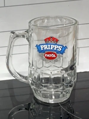 Pripps Fatöl ölsejdel i glas - Klassisk ölsejdel i tjockt, transparent glas med Pripps Fatöl-logga i blått och rött framtill. Robust handtag och mönstrad botten ger en retro känsla. Perfekt för att servera öl hemma eller till samlaren av bryggeriprylar.