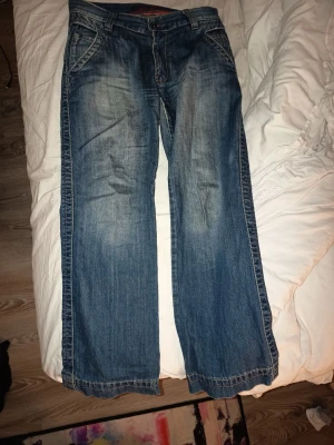 Blåa wide leg jeans  - Säljer ett par blåa jeans med breda ben och snyggt slitna detaljer. Jeansen har klassisk femficksdesign, orangea sömmar och normal midja. Perfekta för dig som gillar en avslappnad och trendig stil.