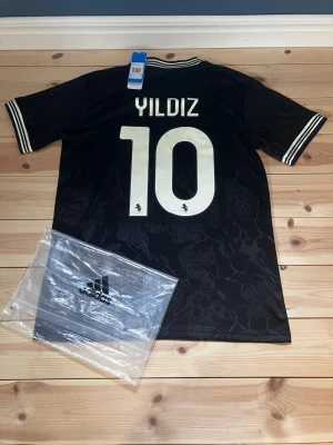 Svart Juventus Yildiz tröja Adidas - Snygg svart Juventus matchtröja från Adidas med Yildiz och nummer 10 på ryggen. Tröjan har vita detaljer, tryckta loggor och blommönster i tyget. Jeep och Visit Detroit som sponsortryck på framsidan. Tillverkad i Aeroready-material för bra ventilation.