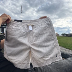 Vita manchester shorts Polo Ralph Lauren - Snygga helt nya vita manchester shorts från Polo Ralph Lauren med diskreta smala ränder och klassisk broderad logga. Nyskick utan lappar. Modellen har elastisk midja med snörning och sidofickor, samt bakfickor. Perfekta för en chill sommardag. Nypris 1795kr.