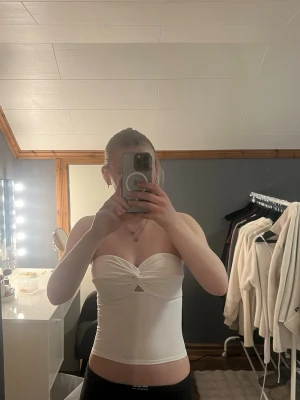 Vit bandeau tubtopp från Bik Bok - Snygg vit bandeau tubtopp från Bik Bok med twistad detalj framtill och liten cut-out under bysten. Toppen är axelbandslös och har en tight passform. 