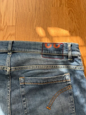 Dondup Jeans - Säljer ett par blå skinny jeans med cool CC-detalj på bakfickan. Jeansen har klassiska bakfickor och snygga sömmar i orange. Perfekt för dig som gillar en slim fit och vill ha något som sticker ut lite.