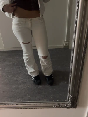 Vita slitna jeans med bootcut - Säljer ett par vita jeans med bootcut och slitningar på knäna. Jeansen har klassisk femficksdesign och är tillverkade i denim. Snygga broderade detaljer på bakfickorna. Perfekta för dig som gillar en trendig och avslappnad look.