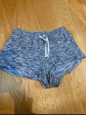 Grå mjuka shorts  - Säljer ett par gråmelerade shorts med snörning i midjan och två sidofickor. De är tillverkade i ett mjukt och bekvämt material, perfekta för sommarens dagar. Passformen är normal och de har en elastisk midja för extra komfort. Barnstrolek 134/140 men passar även xxxs/xxs.