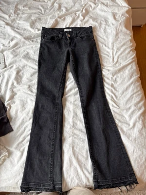 Svarta bootcut jeans  - Snygga svarta bootcut jeans med klassiska fem fickor. Jeansen har låg midja och silverfärgade knappar på bakfickorna. Byxorna är uppsprättade längst ner .
