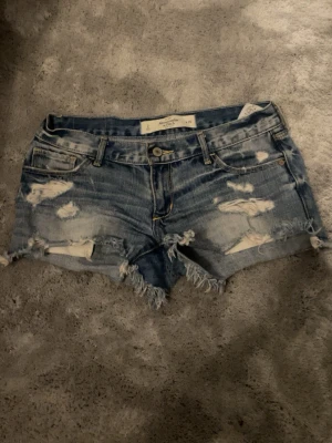 Lågmidjade Abercrombie & fitch jeansshorts - Säljer nu mina älskade eftertraktade vintage Abercrombie & fitch jeansshorts med slitningar pga för stora🥹🥹köpte på Sellpy för ca 650kr!! Midjemått runt om är ca 78cm