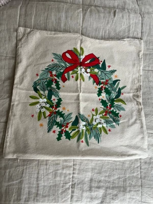 4st kuddfodral med julmotiv - Säljer 4st kuddfodral i beige med tryckt julkrans i grönt, rött och vitt. Kransen har detaljer som röda bär, gröna blad och en stor röd rosett. Perfekt för att skapa mysig julstämning i soffan eller sängen.
