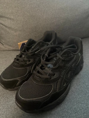 Svarta Asics sneakers - Säljer ett par helsvarta Asics sneakers med cool chunky sula. Ovandelen är i mesh och syntetläder för både stil och komfort. Klassisk snörning och diskret logga på sidan. Perfekta för dig som gillar sportig streetstyle. Helt nya! Kommer ej med box för har tappat bort den😅