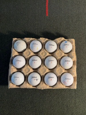 12 vita Titleist golfbollar  - Säljer ett set med 12 vita golfbollar från Titleist. Bollarna har klassisk dimple-design och är märkta med olika siffror och små färgmarkeringar. Perfekt för dig som vill fylla på golfbagen inför säsongen.
