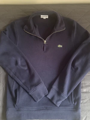 Mörkblå half-zip tröja från Lacoste - Mörkblå långärmad tröja från Lacoste. Har inga defekter och inga hål, passformen är regular och passar mer S/M även om det står M. Kom dm för fler bilder och om ni har frågor