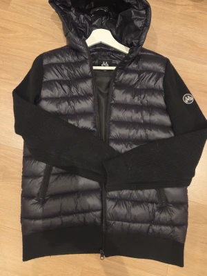 Maggiore cardigan - Snygg svart cardigan från Maggiore med stickade ärmar och vadderad kropp. Jackan har huva, dragkedja framtill och två fickor med dragkedja. Maggiore-logga på ärmen. Perfekt för dig som gillar att ha en clean outfit men grish-vibe känsla. Den är använd 1 gång och Tveka inte på att diskutera pris, eller bara har frågor. 🙏🏼✨️